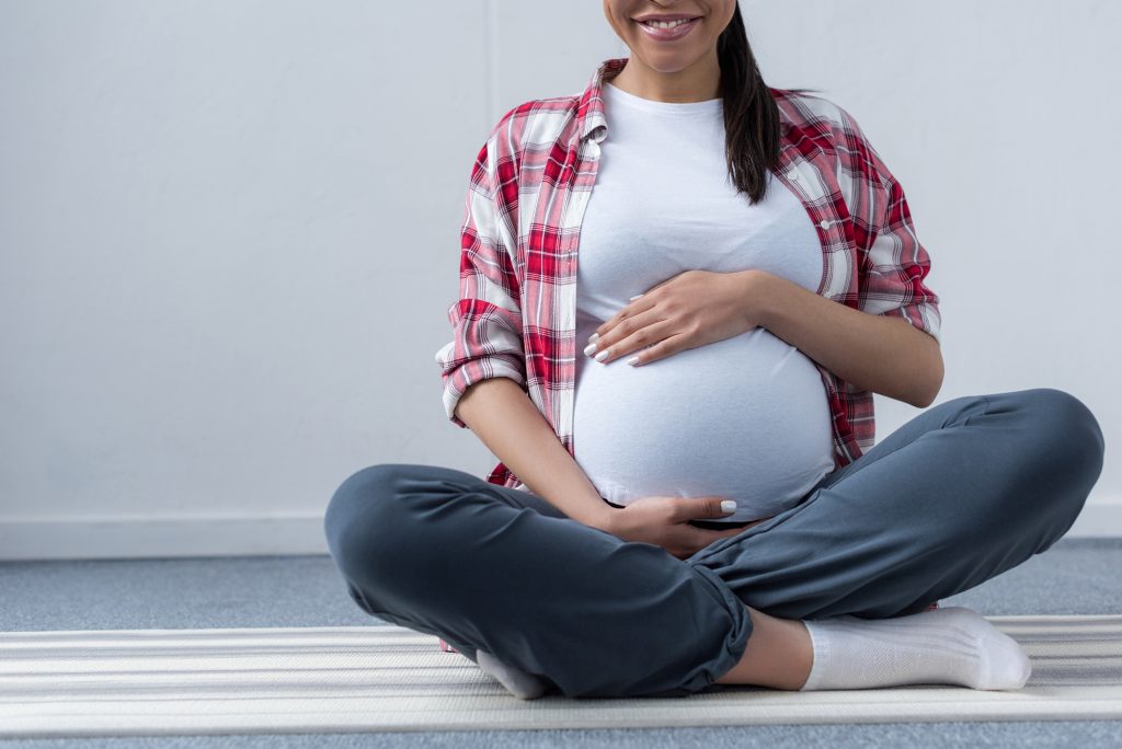 Pregnant mom sitting cross-legged on the ground smiling